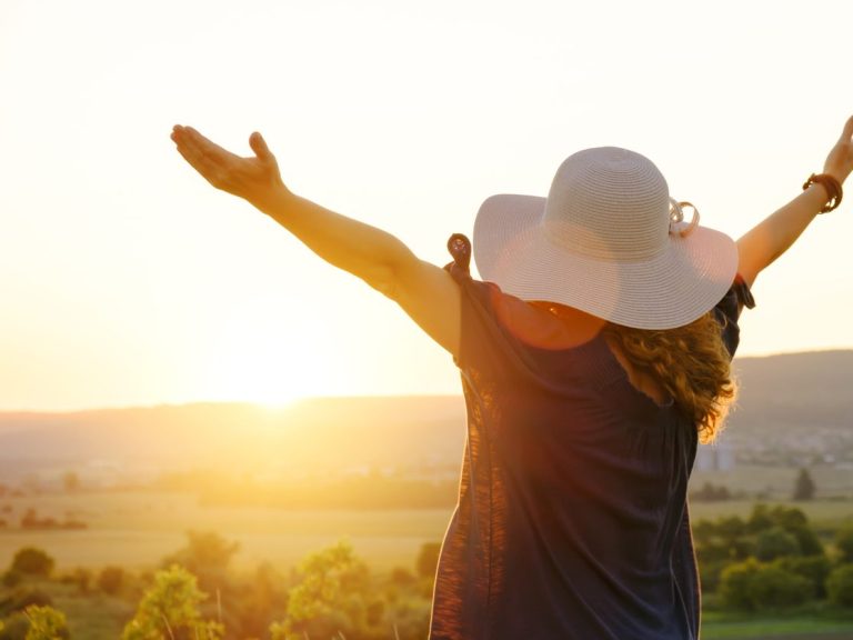 Frau sitzt am Ufer eines Sees und genießt den Sonnenaufgang mit einer Tasse Tee in der Hand.